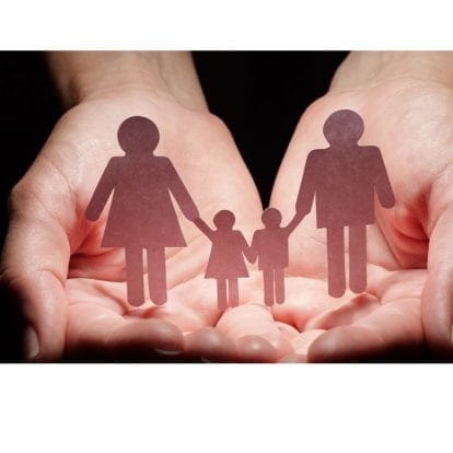 pair of hands holding shadowed paper cutouts of a family with two children