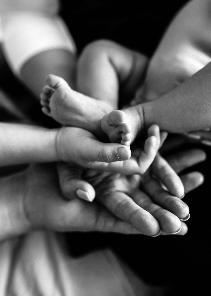 photo of two sets of adults hand cradling a baby's feet.