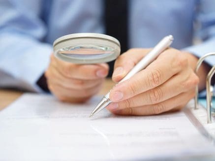 man holding magnifying glass and pen while checking a document