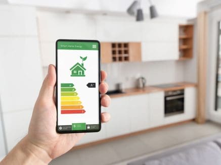interior image of a kitchen with a person holding up a phone, the screen showing an energy efficiency graph and an image of a green coloured house denoting an energy efficient home
