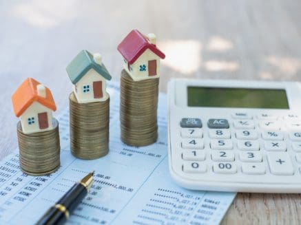 Image of three houses stagcked on coins with paperwork pen and calculator nearby denoting tax on residential property sales