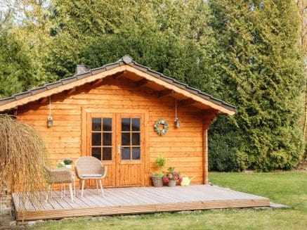 wooden summerhouse in a garden with table cnd chairs in front of it