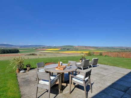 Rural screne of an oudroor table and chairs with a bottle of wine and two glasses with glorious views across the NE Scotland countryside.