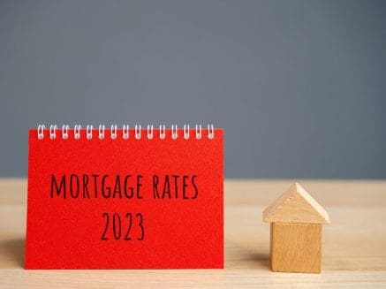 red sign with words mortgage rates 2023 written and a wooden block house next to it, denoting mortgage interest rates in 2023